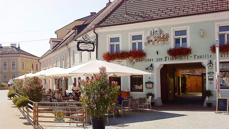 Braugasthaus zum Fiakerwirt, © Braugasthaus zum Fiakerwirt Außenansicht eines traditionellen Gasthauses mit Terrasse und Sonnenschirmen.