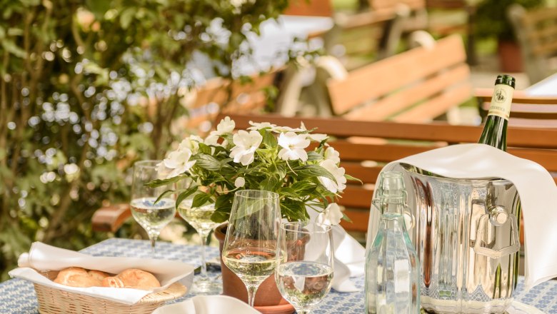 Garten Loibnerhof, © Rita Newman Gedeckter Tisch im Garten mit Blumen, Wein und Wasser.