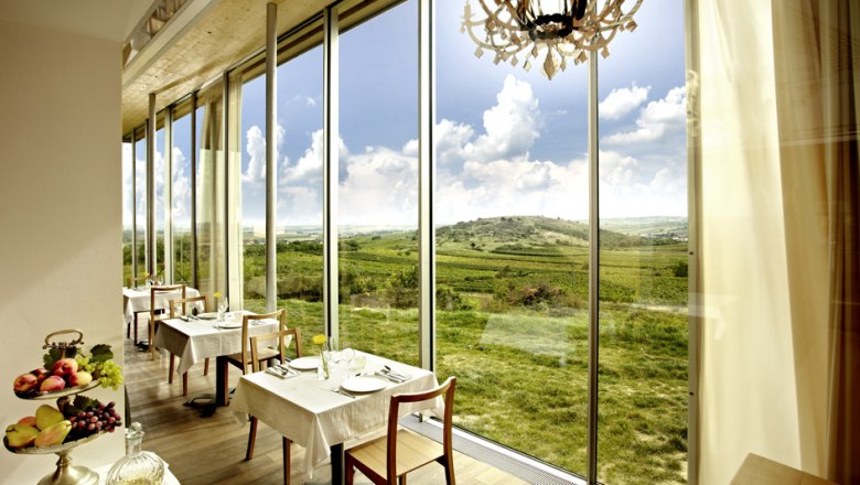 Windmühlheuriger Bergmann, © Alexander Schleissing Innenansicht eines Restaurants mit großen Fenstern und Blick auf eine grüne Landschaft.