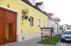 Weinbau Buschenschank Gästezimmer Susanna Poys, © Familie Poys Gelbes Gebäude mit Schild 'Gästezimmer Buschenschank Weinbau Poys' und geparktem Auto davor.