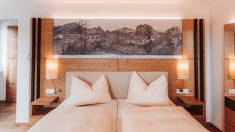 Premium Doppelzimmer mit Balkon, © Payerbacherhof - Christopher Tarkus Ein modernes Doppelzimmer mit zwei Betten, Holzmöbeln und einem Landschaftsbild über dem Bett.