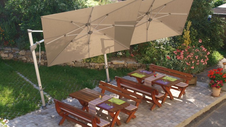 Frühstücksterrasse, © Weidenauer Holztische und Bänke auf einer Terrasse mit Sonnenschirmen, umgeben von Blumen und Grün.
