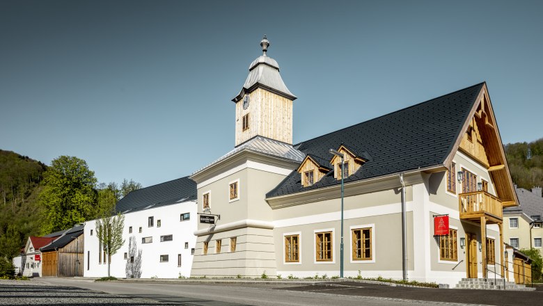 Hotel zum Glockenturm, © croce&wir Ein modernes Gebäude mit Glockenturm und Holzverkleidung, umgeben von Bäumen und klarem Himmel.