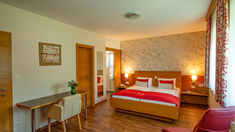 Zimmer im Hotel Weinquadrat, © ivan-lukacic-photography Hotelzimmer mit Doppelbett, Schreibtisch, Stuhl und rotem Sessel.