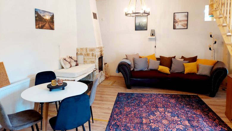 Wohn-Esszimmer, © Wein-Bleibe Gemütliches Wohn-Esszimmer mit Holzbalken, Sofa, Esstisch und Kamin.