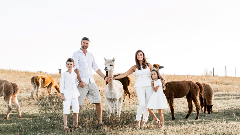 Familie Widhalm, © Andreas Widhalm Eine Familie in weißer Kleidung steht auf einer Wiese mit Alpakas.
