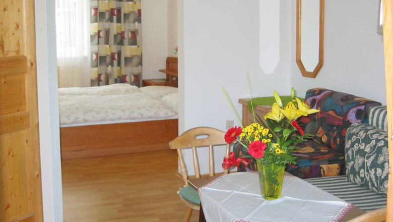 Gasthof Neumeister, © MG Rfd Ein gemütliches Zimmer mit Holzmöbeln, einem Bett im Hintergrund und einem Tisch mit Blumen im Vordergrund.