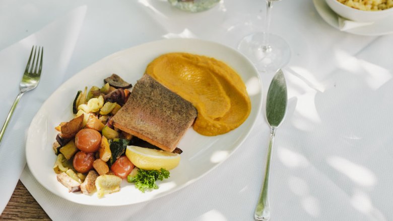 Fisch vom „Gut Dornau“, © Niederösterreich Werbung/Michael Reidinger Gedeckter Tisch mit Fischgericht, Gemüse und Püree, Weißwein im Hintergrund.