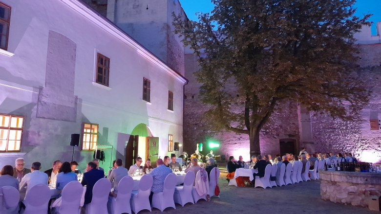 Tafeln im Weinviertel, © Weinviertel Tourismus GmbH Abendessen im Freien mit langen Tischen und Stühlen in einem historischen Innenhof.