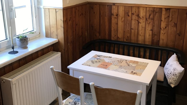 Essecke in der Küche, © Martina Braun Kleine Essecke mit Tisch, Stühlen und Bank in einer Küche mit Holzvertäfelung.