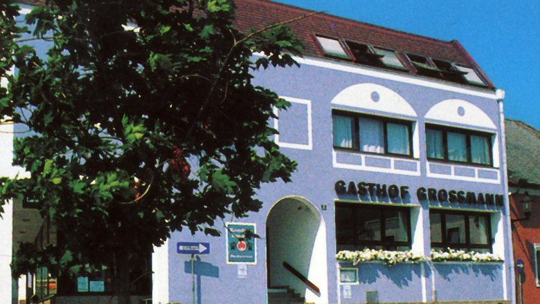 Gasthof Gro&szlig;mann mit blauer Fassade und Baum im Vordergrund.