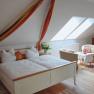 Gem&uuml;tliches Schlafzimmer mit Doppelbett, Sesseln und Tisch unter Dachschr&auml;ge.