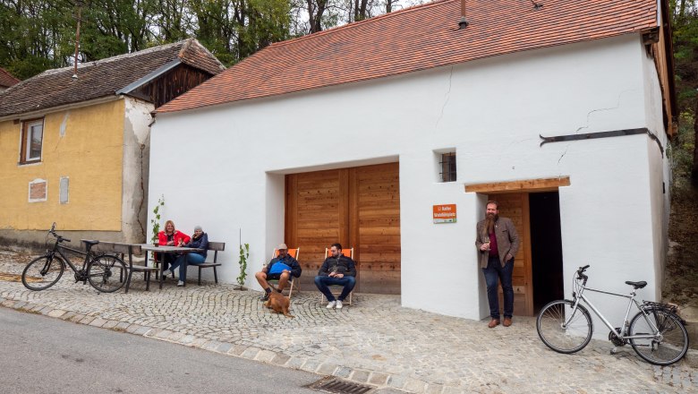 Menschen sitzen vor einem Kellergeb&auml;ude mit Fahrr&auml;dern.