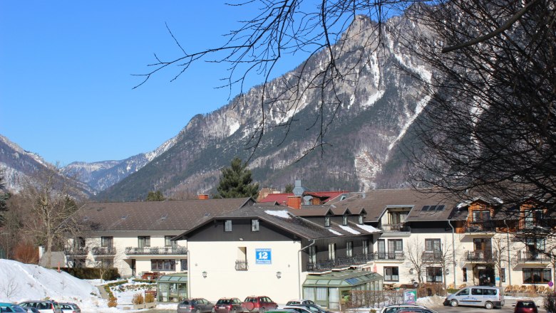 Au&szlig;enansicht eines Geb&auml;udes vor einer Bergkulisse mit schneebedeckten Gipfeln und blauem Himmel.