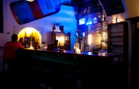 Innenansicht einer Bar mit blauer Beleuchtung und Flaschenregalen.