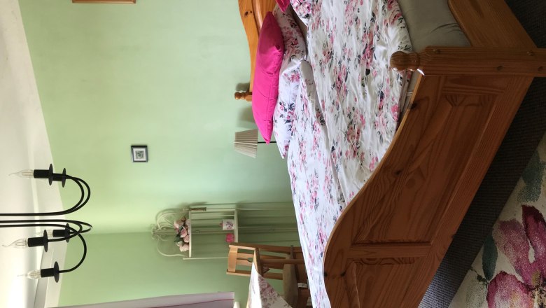 Schlafzimmer mit Doppelbett, grüne Wände, Blumenbettwäsche, Tisch mit Stühlen, Vorhänge und Kronleuchter.