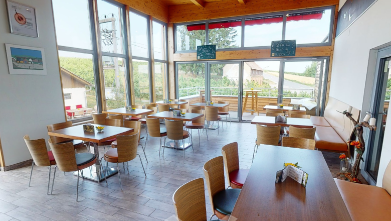 Innenansicht eines modernen Heurigen mit Holzm&ouml;beln und gro&szlig;en Fenstern.