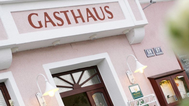 Gasthaus mit Gästehaus, © Familie Bsteh Eingang eines Gasthauses mit rosa Fassade und Beschilderung.