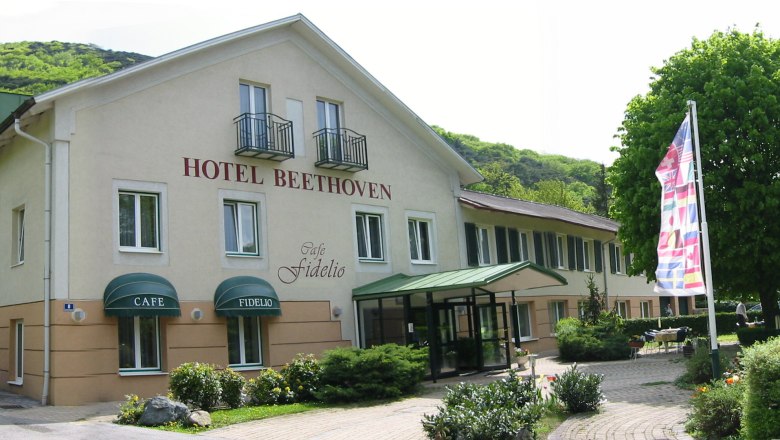 Au&szlig;enansicht des Hotel Beethoven mit Caf&eacute; Fidelio, umgeben von B&auml;umen und Flaggen.