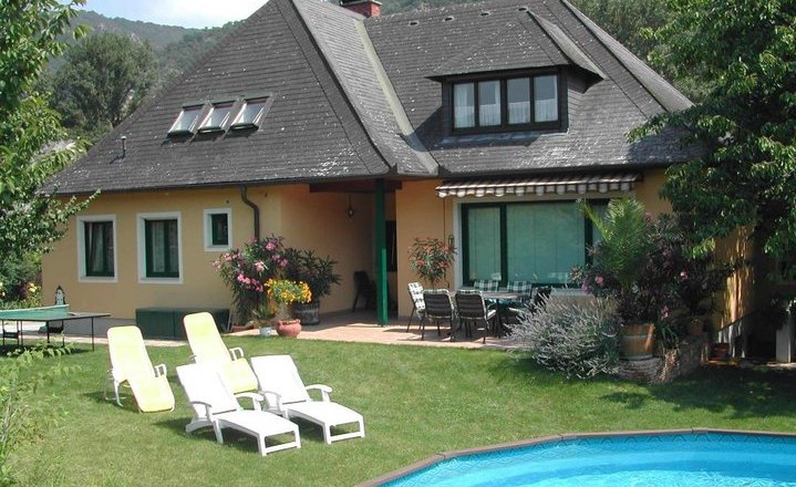 Ein Haus mit Garten, Pool und Liegestühlen.