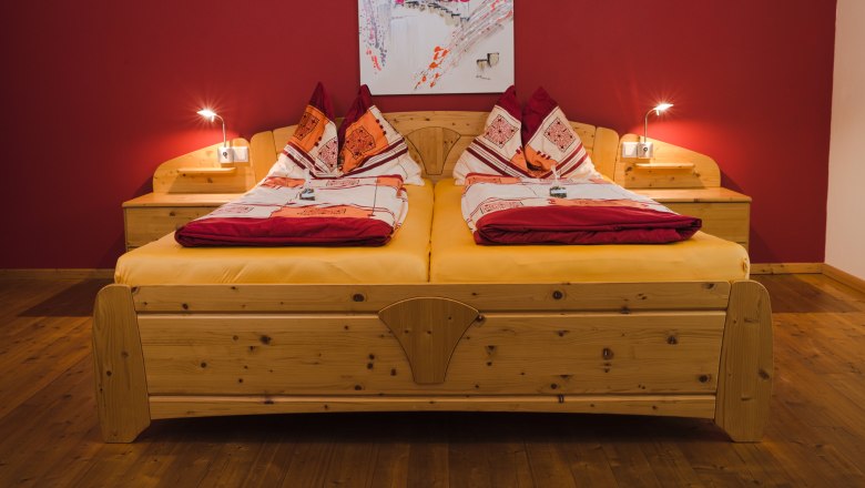 Gem&uuml;tliches Doppelbett mit roter Wand und Holzfu&szlig;boden.