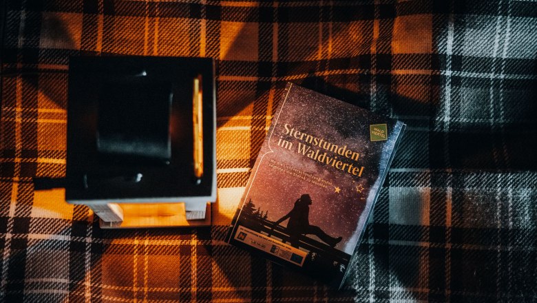 Ein Buch mit dem Titel 'Sternstunden im Waldviertel' liegt auf einer karierten Decke neben einer Laterne.