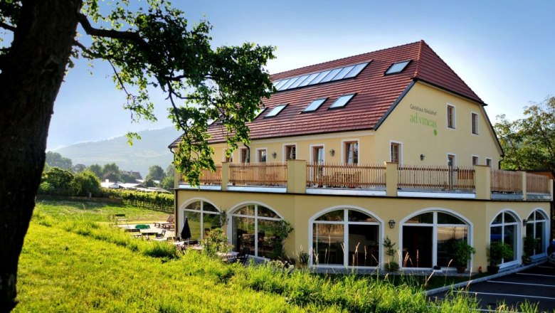 Gelbes Geb&auml;ude mit rotem Dach und Terrasse, umgeben von gr&uuml;ner Landschaft.