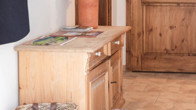 Ein Vorraum mit Holzm&ouml;beln, einem Korb, Stiefeln und einer Vase mit Blumen.