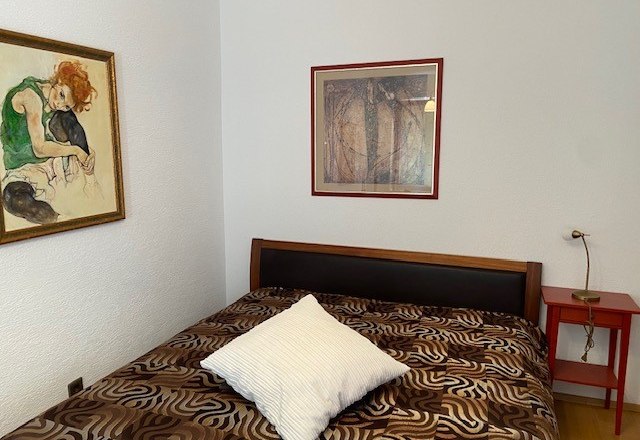 Ein Schlafzimmer mit einem Bett, zwei gerahmten Bildern an der Wand und einem roten Nachttisch.