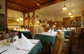 Innenansicht eines gemütlichen Wirtshauses mit Holzmöbeln und gedeckten Tischen.