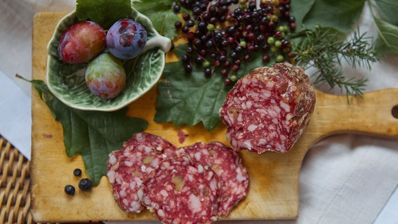 Nahaufnahme einer Salami auf einem Holzbrett mit Beeren und Pflaumen.