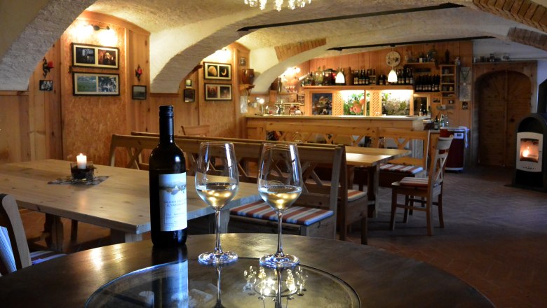 Gem&uuml;tlicher Weinkeller mit Holzm&ouml;beln, Weinflasche und Gl&auml;sern auf einem Tisch.