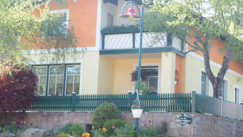 Ein zweistöckiges Haus mit orange-gelber Fassade, grünem Zaun und Garten.