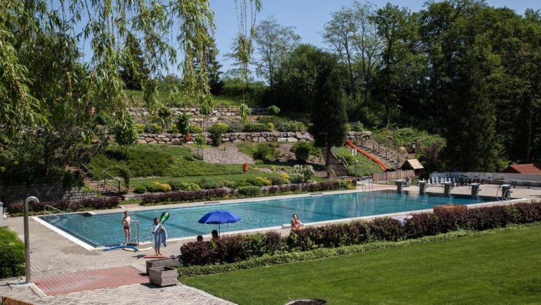 Ein Freibad mit Schwimmbecken, umgeben von B&auml;umen und Rasenfl&auml;chen.