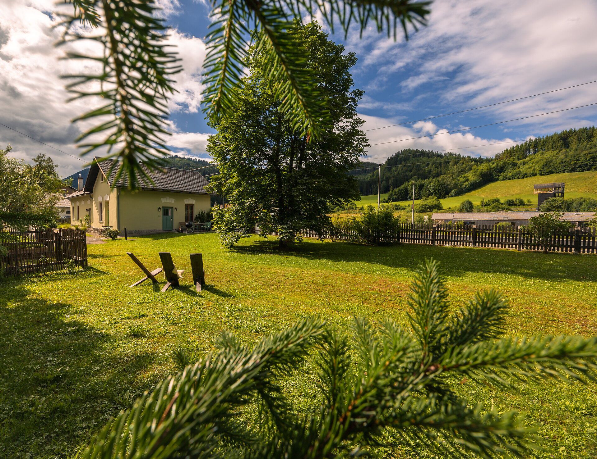 Ein goldener Zug hält am Bahnhof Wienerbruck-Josefsberg, umgeben von grüner Landschaft und einem kleinen Sitzbereich im Freien.