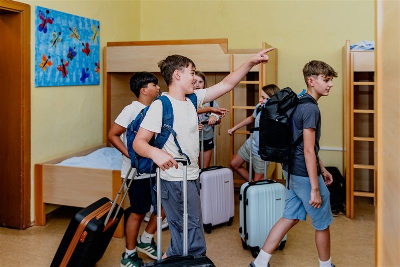 Gruppe von Kindern mit Koffern in einem Schlafsaal mit Etagenbetten.