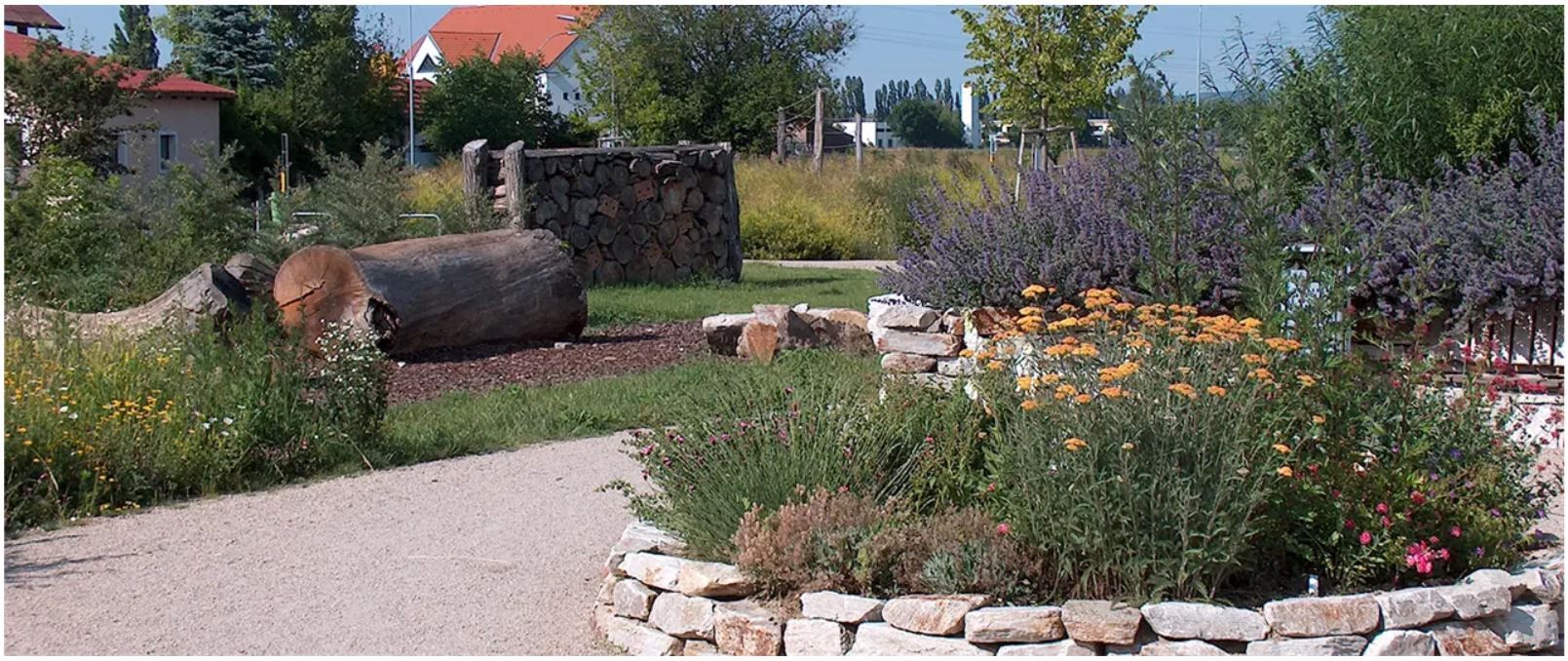Ein gepflegter Garten mit Blumen, Bäumen und einem Holzstapel.