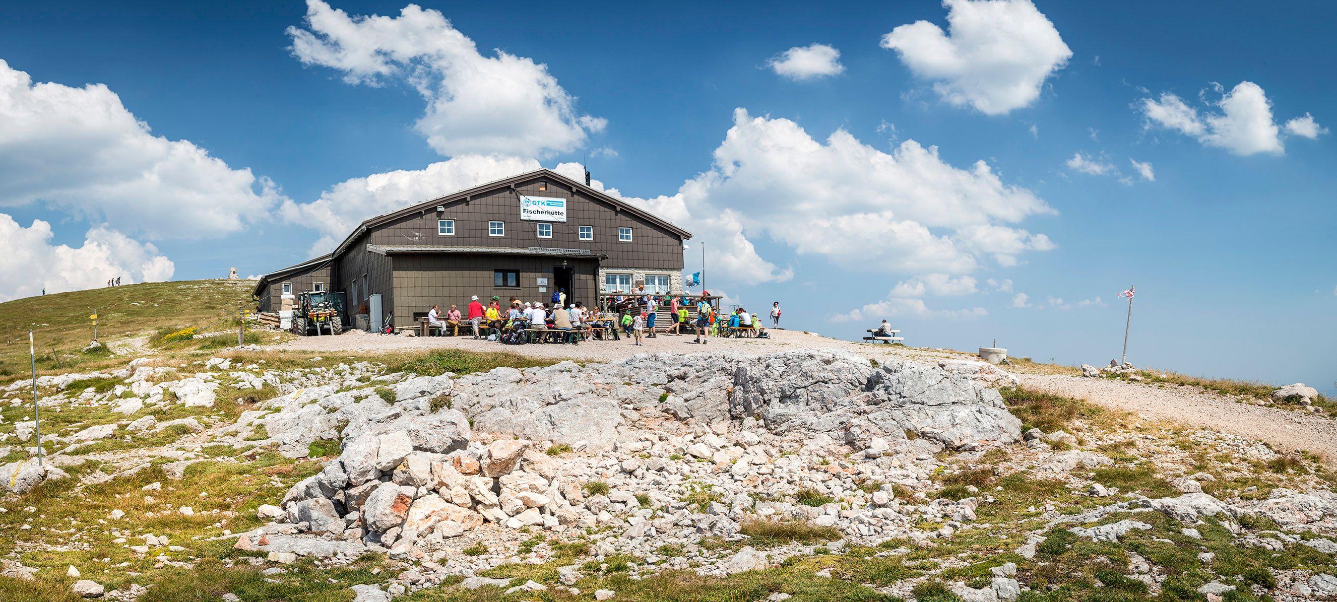 Fischerhütte auf dem Schneeberg mit Wanderern und blauem Himmel.