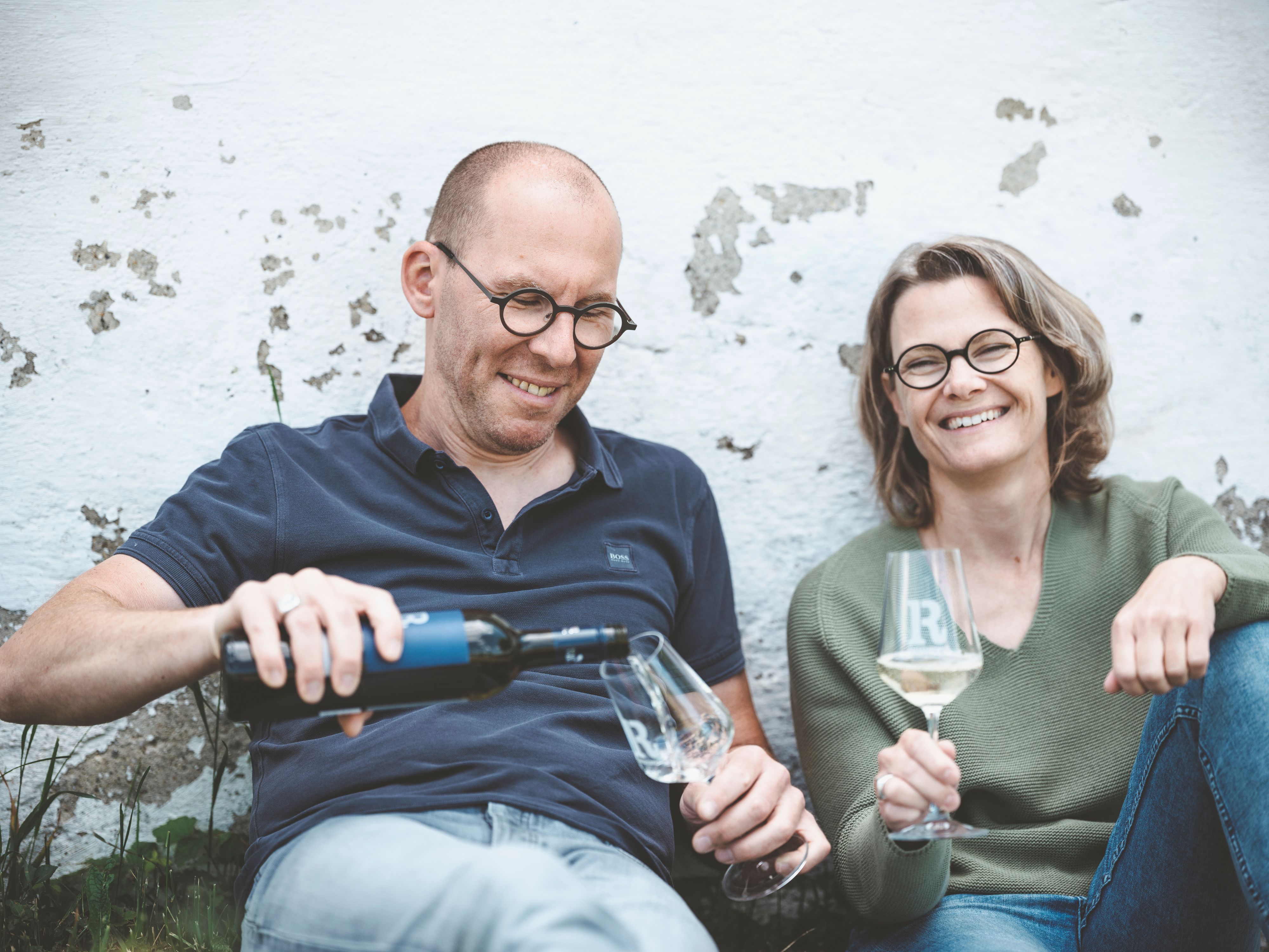 Zwei Personen sitzen entspannt an einer Wand und trinken Wein.