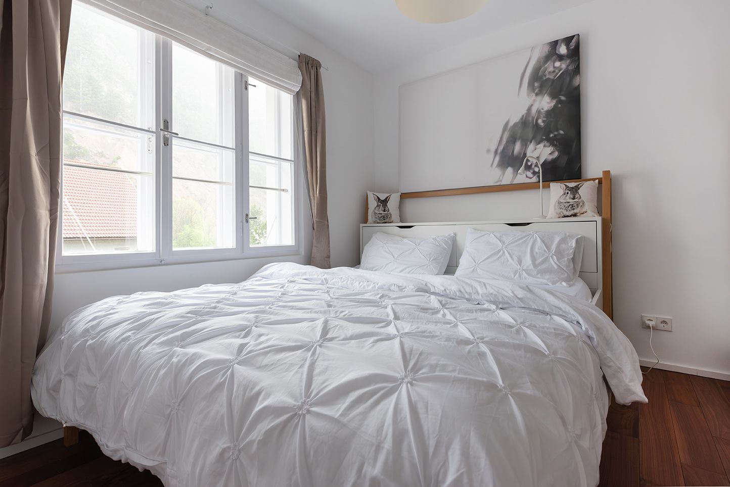 Helles Schlafzimmer mit großem Bett und weißen Bettbezügen, Fenster mit Blick nach draußen.