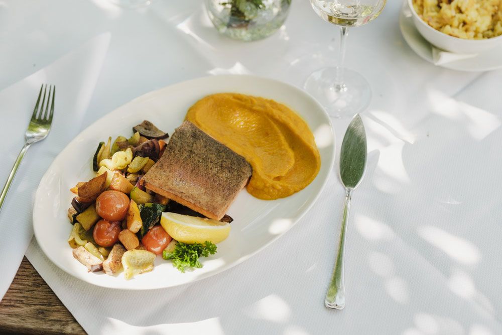 Gedeckter Tisch mit Fischgericht, Gemüse und Püree, Weißwein im Hintergrund.