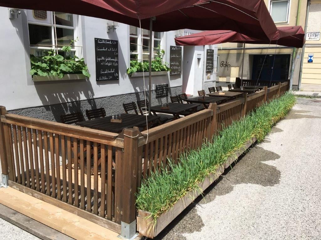 Außenbereich eines Restaurants mit Holzzaun, Tischen und roten Sonnenschirmen.