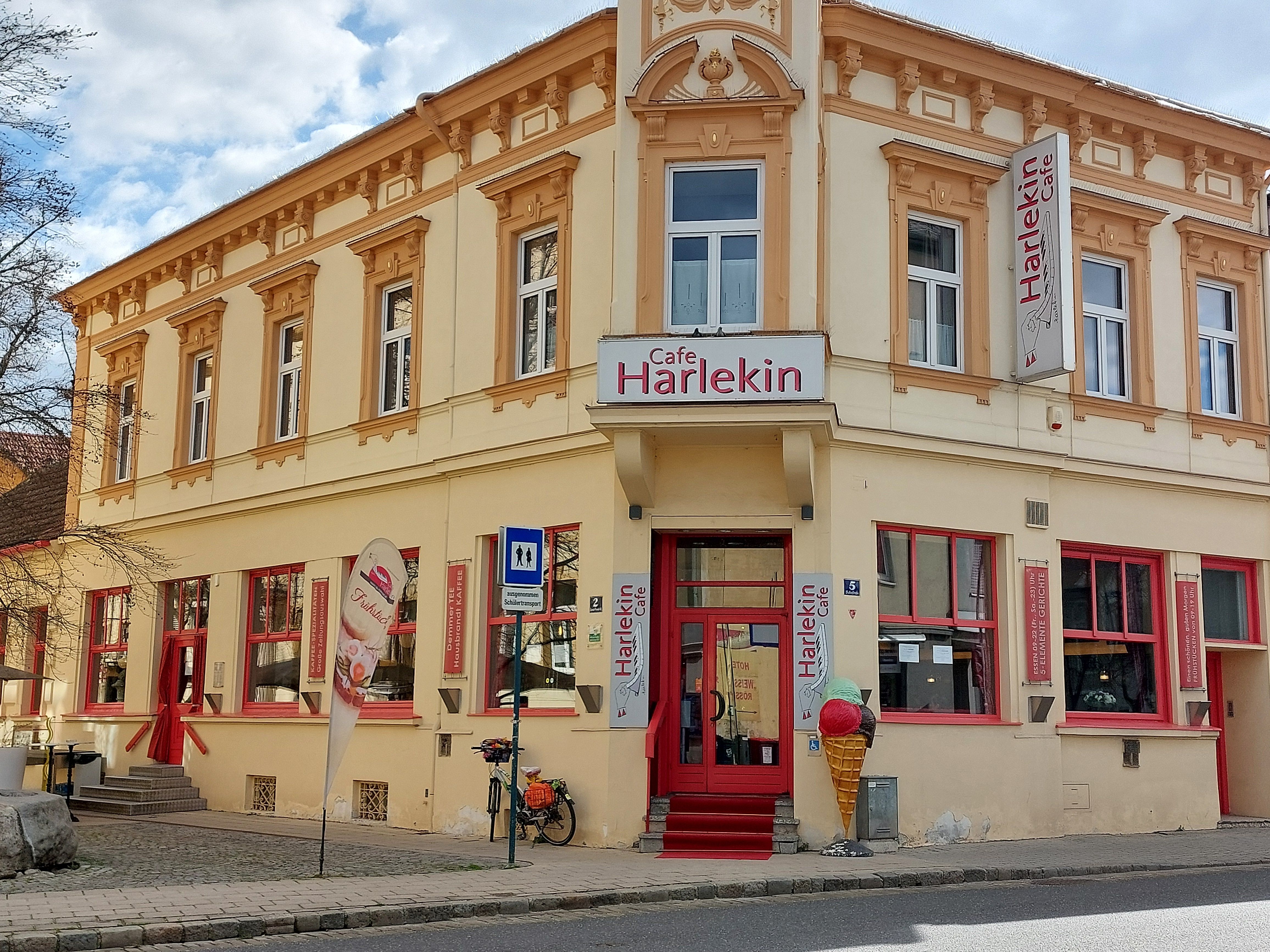 Außenansicht des Cafe Restaurant Harlekin mit gelber Fassade und roten Fenstern.
