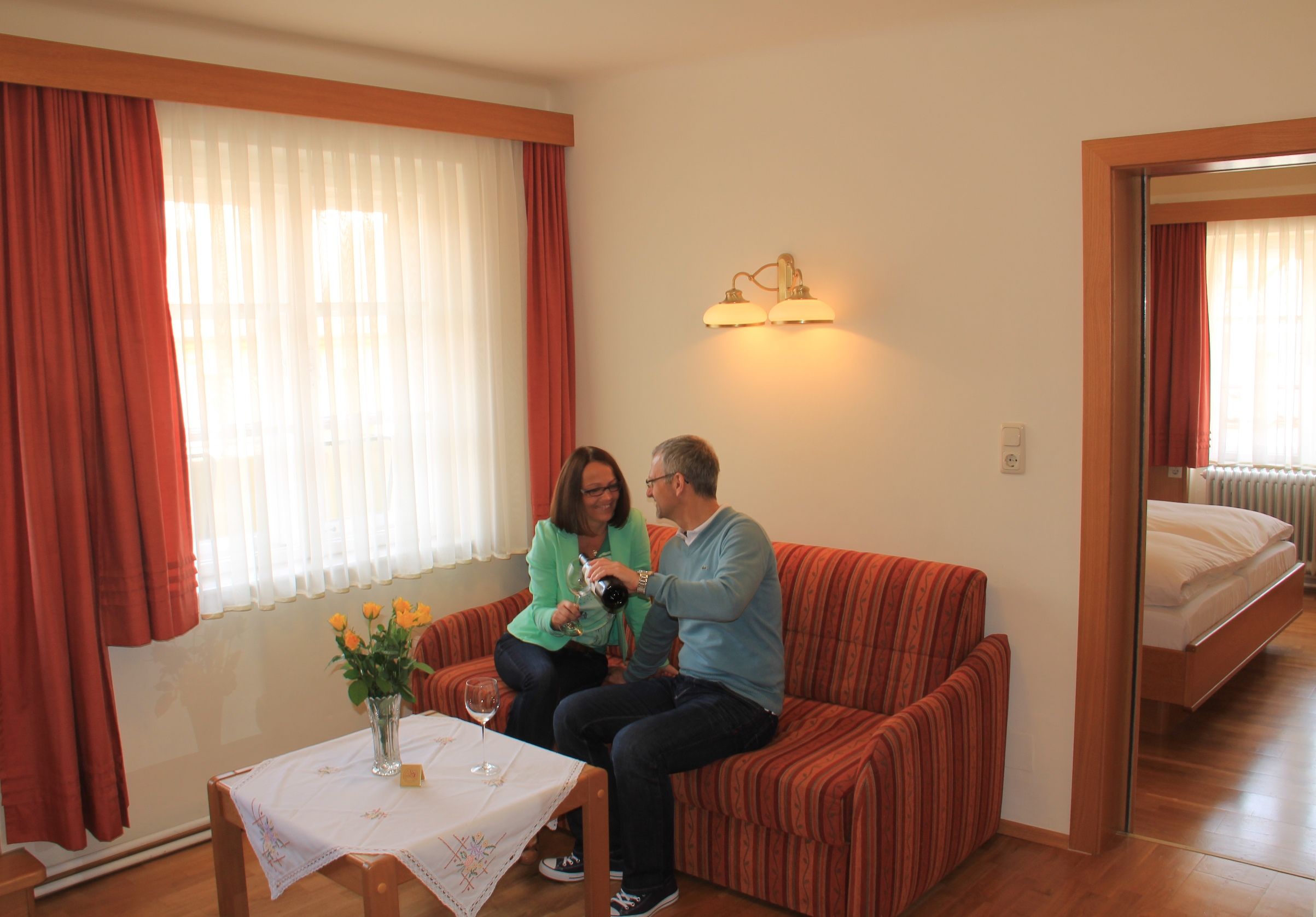 Ein Paar sitzt auf einem Sofa in einem gemütlichen Appartement und schenkt Wein ein.