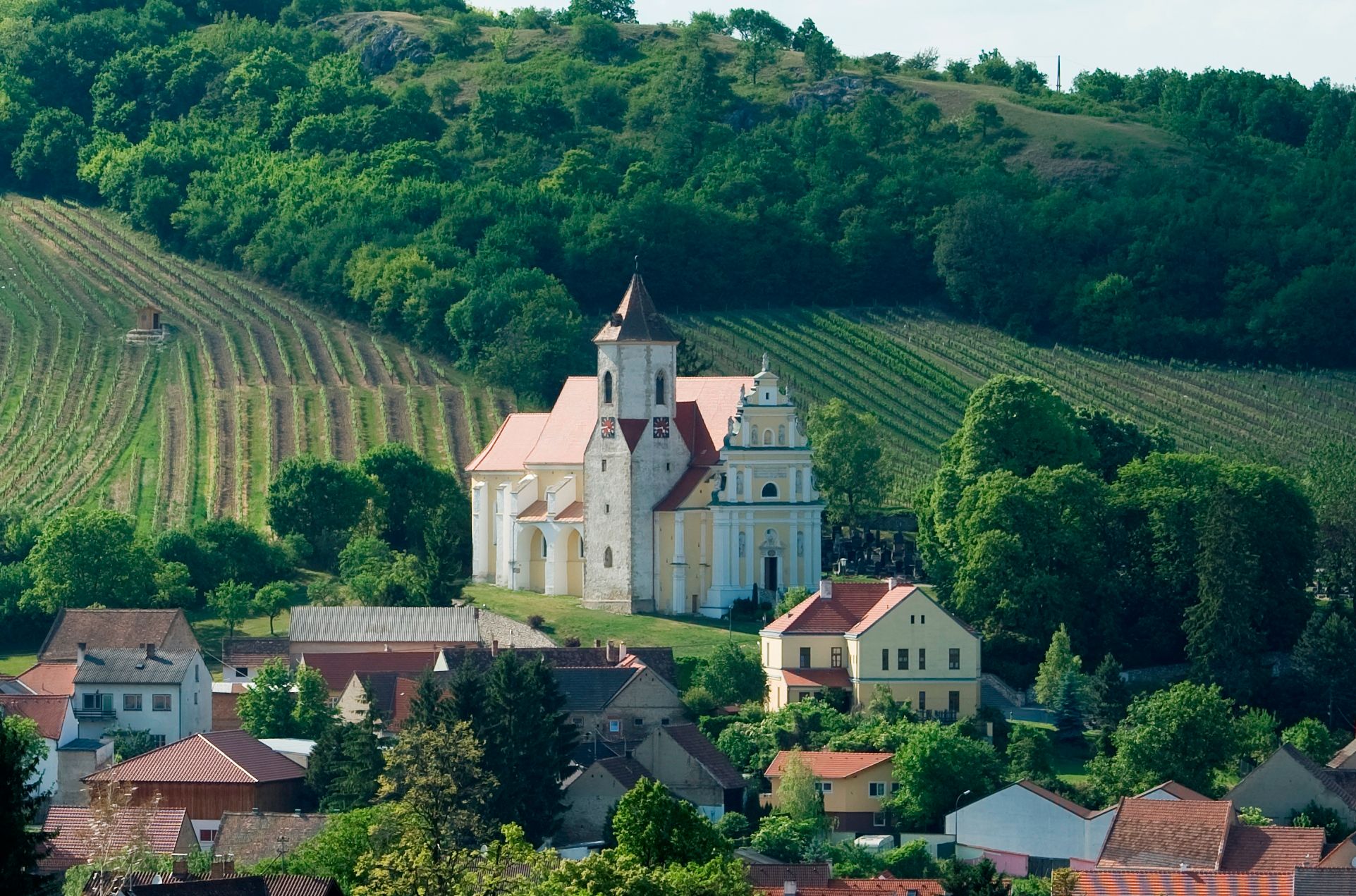 Eine Kirche inmitten von Weinbergen und Häusern, umgeben von grünen Hügeln.
