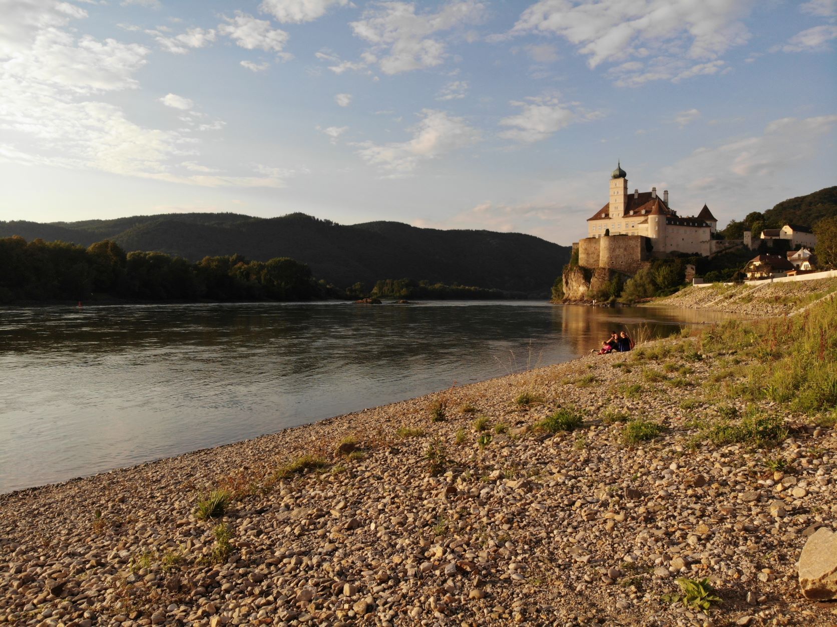 Kiesstrand an der Donau mit Burg im Hintergrund bei Sonnenuntergang.