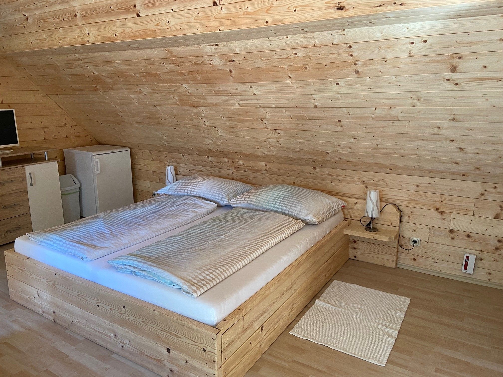 Ein gemütliches Doppelzimmer mit Holzverkleidung, einem Doppelbett, einem kleinen Kühlschrank und einem Fernseher auf einer Kommode.