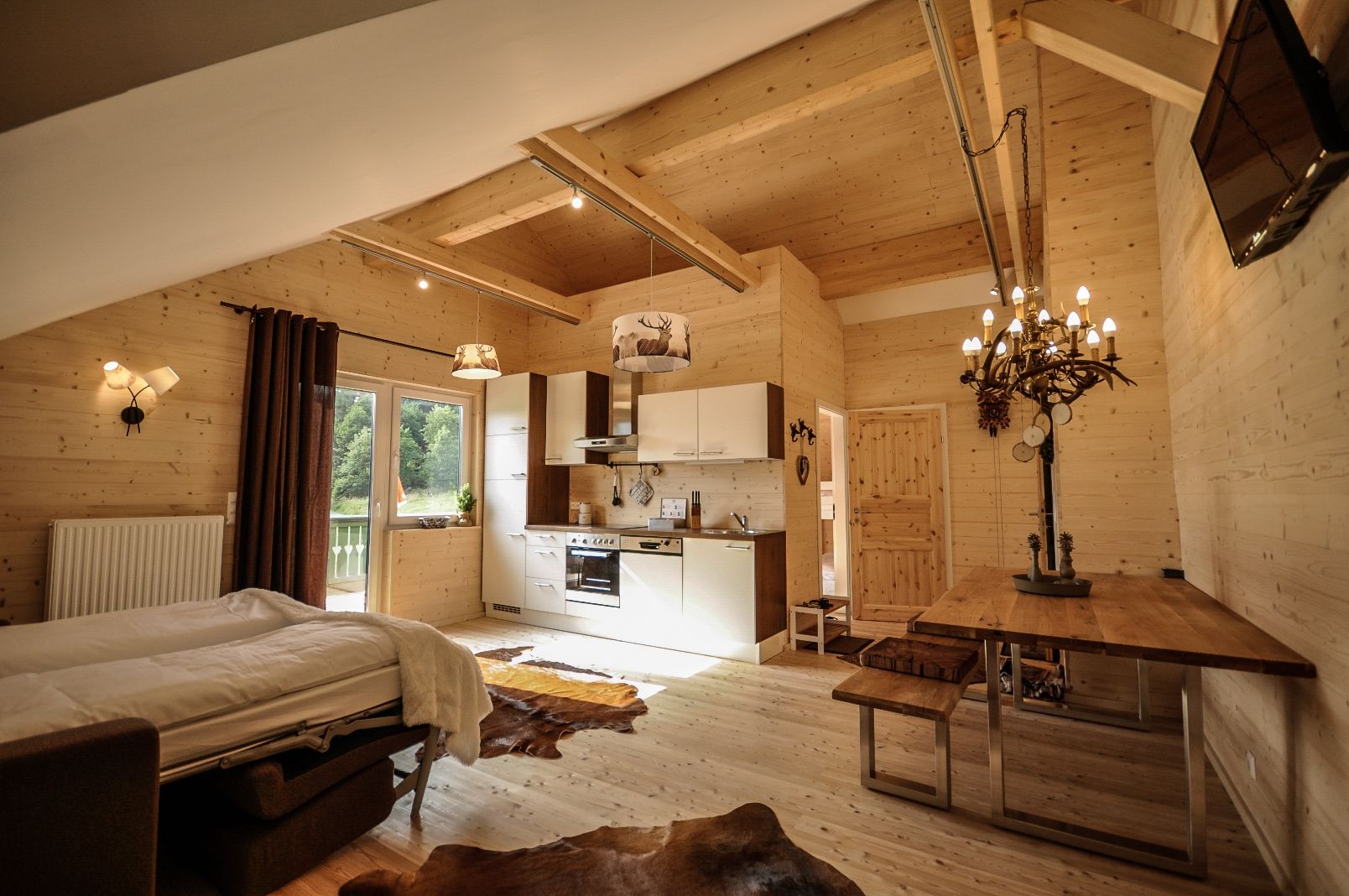 Gemütliches Apartment mit Holzwänden, Küche, Esstisch und Bett.