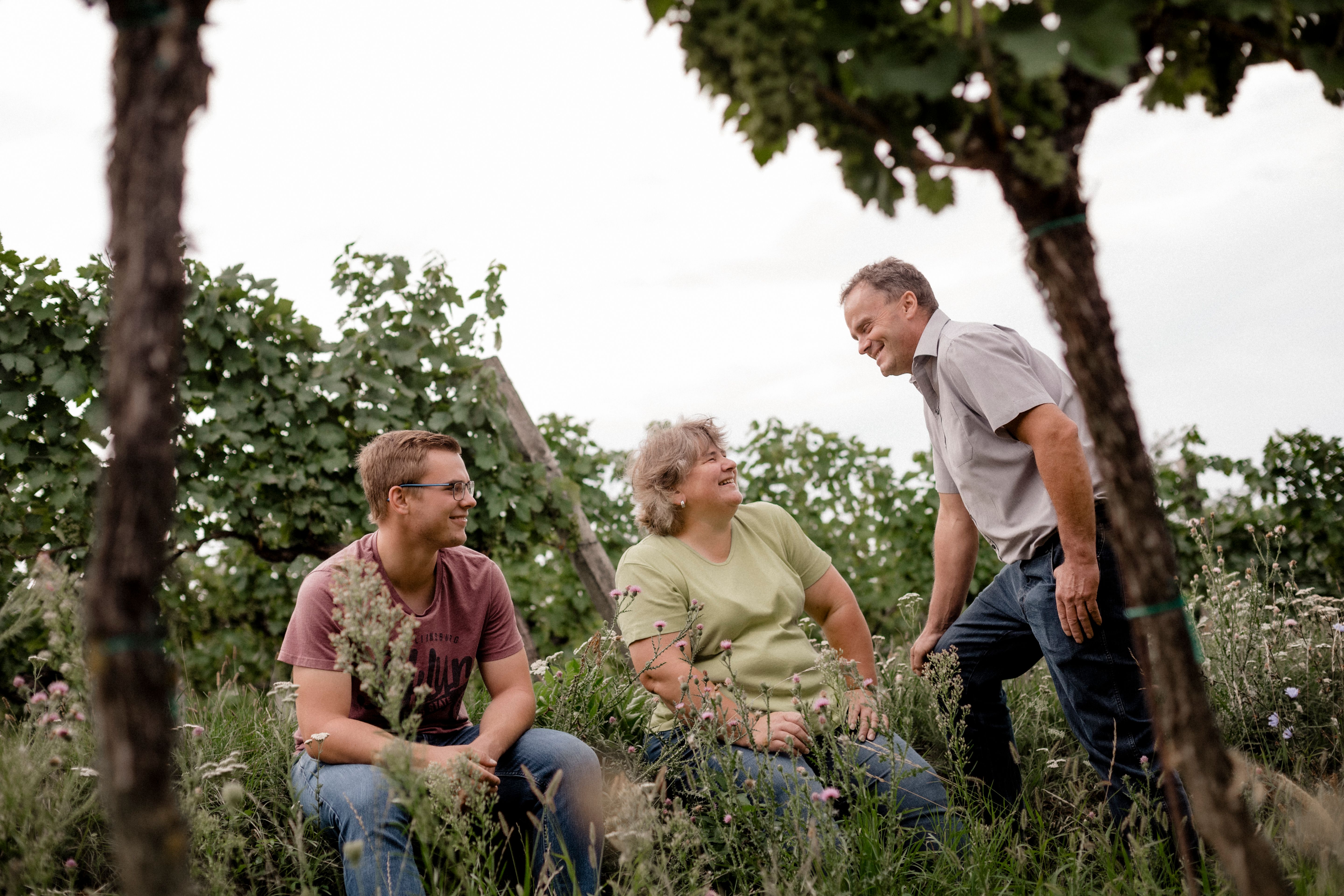 Drei Personen in einem Weinberg, die miteinander lachen.