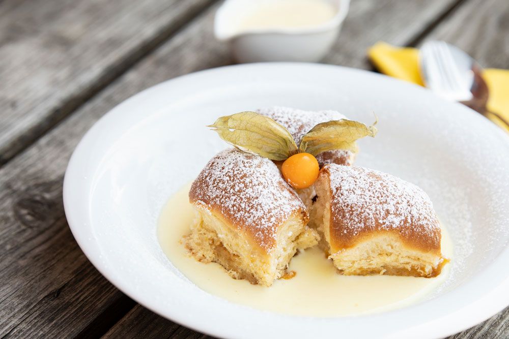 Drei Buchteln mit Puderzucker und Physalis auf Vanillesauce auf einem weißen Teller.